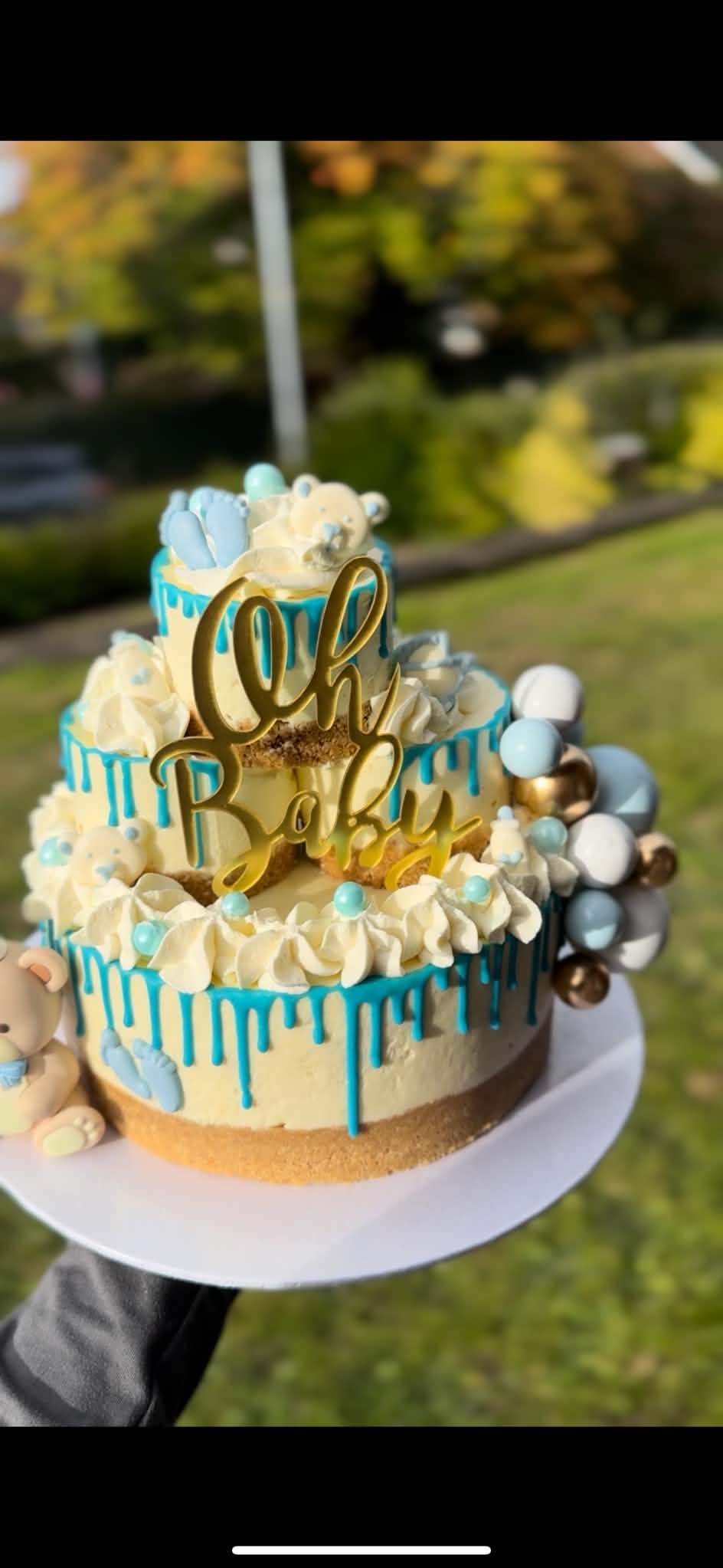 A tiered baby celebration cheesecake with blue drips, teddy bears and a gold Oh Baby topper