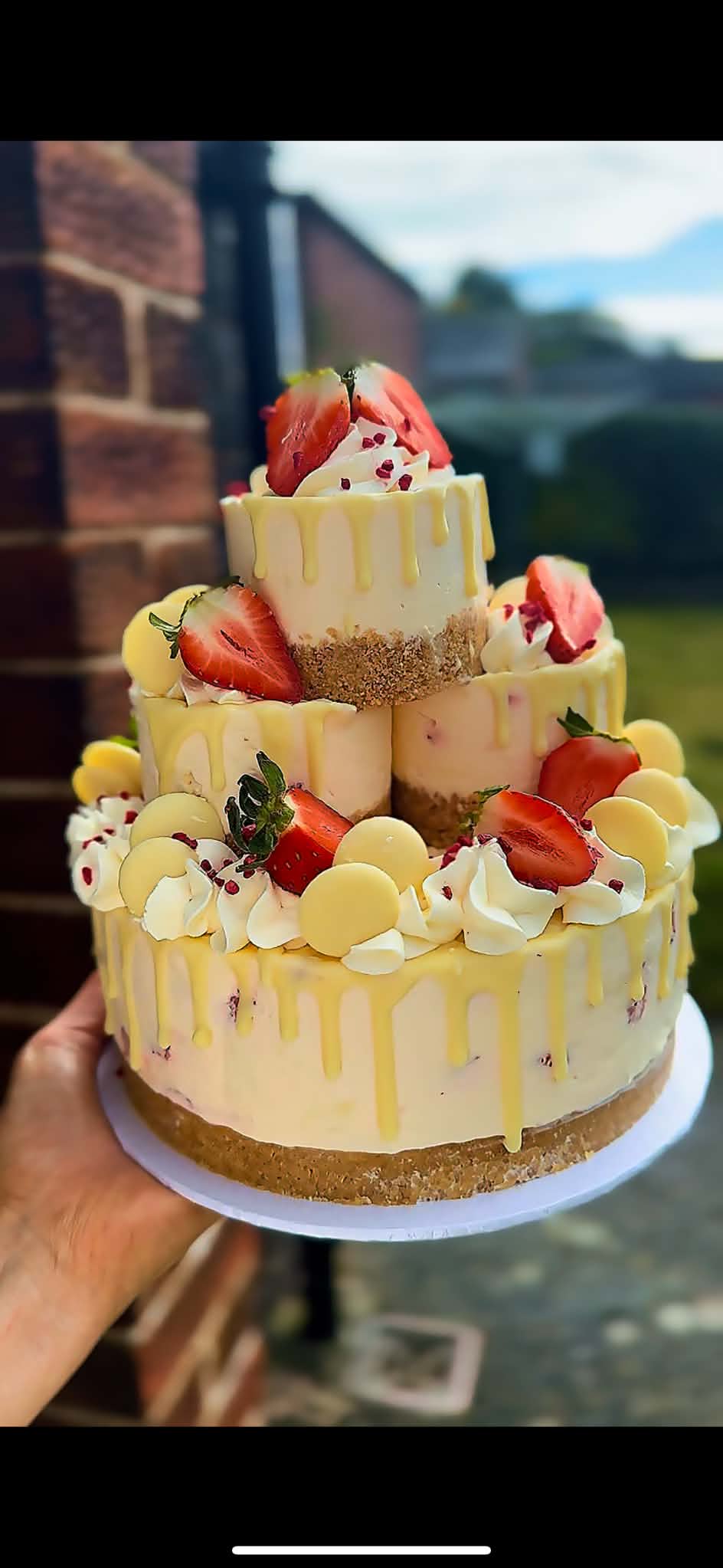A tiered cheesecake decorated with strawberries, cream and yellow drips